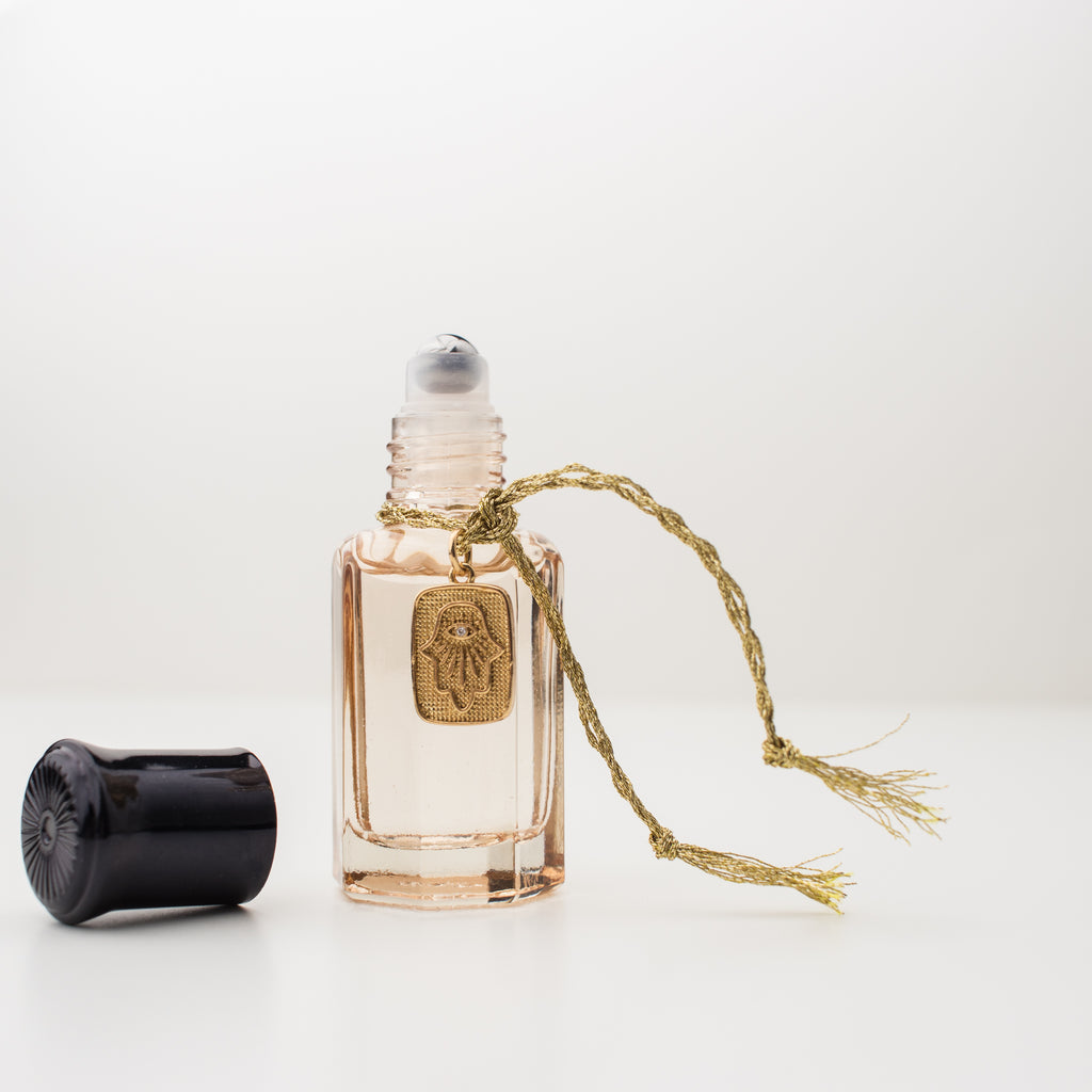 Amuletta's La Mûre fragrance. Blackberry, peach, jasmine, lavender & vanilla. In a blush bottle with a hamsa hand gold filled tag attached with gold braided embroidery thread.