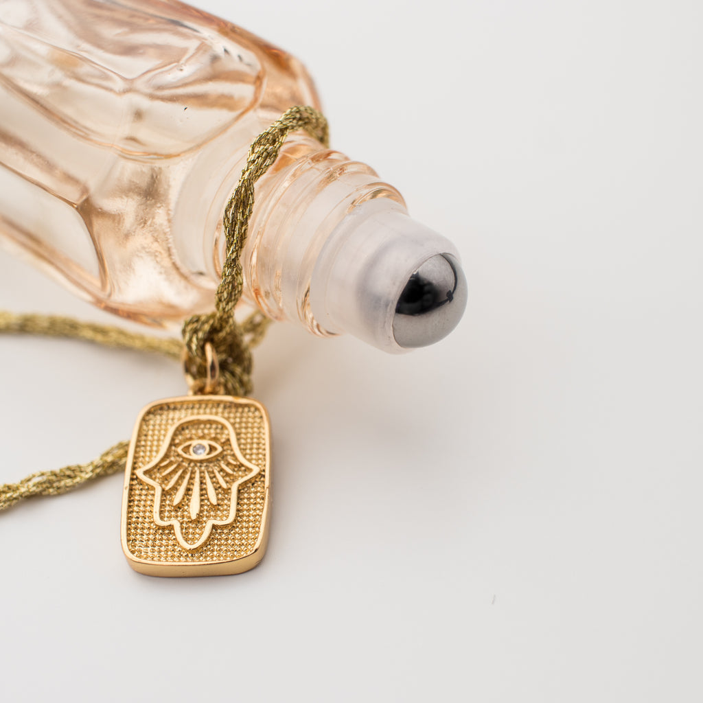 Amuletta's La Mûre fragrance. Blackberry, peach, jasmine, lavender & vanilla. In a blush bottle with a hamsa hand gold filled tag attached with gold braided embroidery thread. Roller tip.