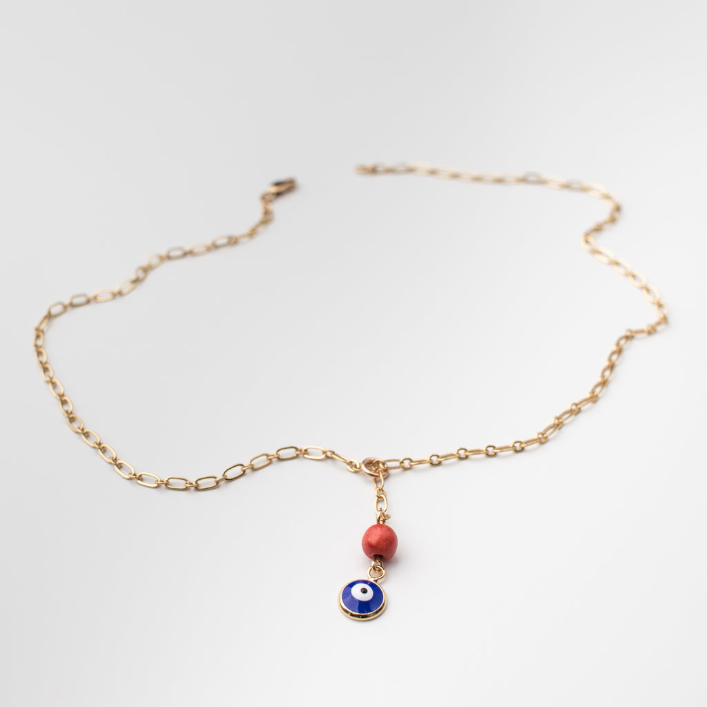 Gold necklace with an enamel cobalt blue eye charm and orange coral bead.