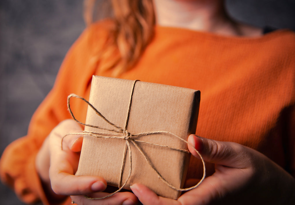Person giving gift of homemade edibles in brown paper wrapping and twine bow..