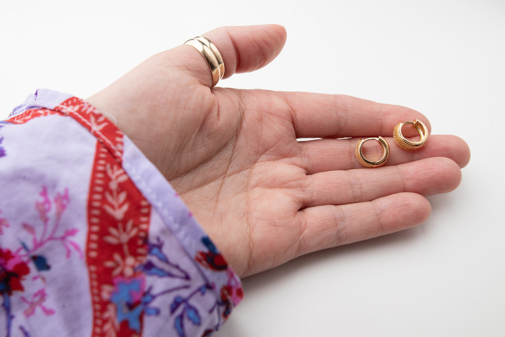 Hand showing the size of a small snake skin texture gold hoop earring that are 5.5 mm thick.