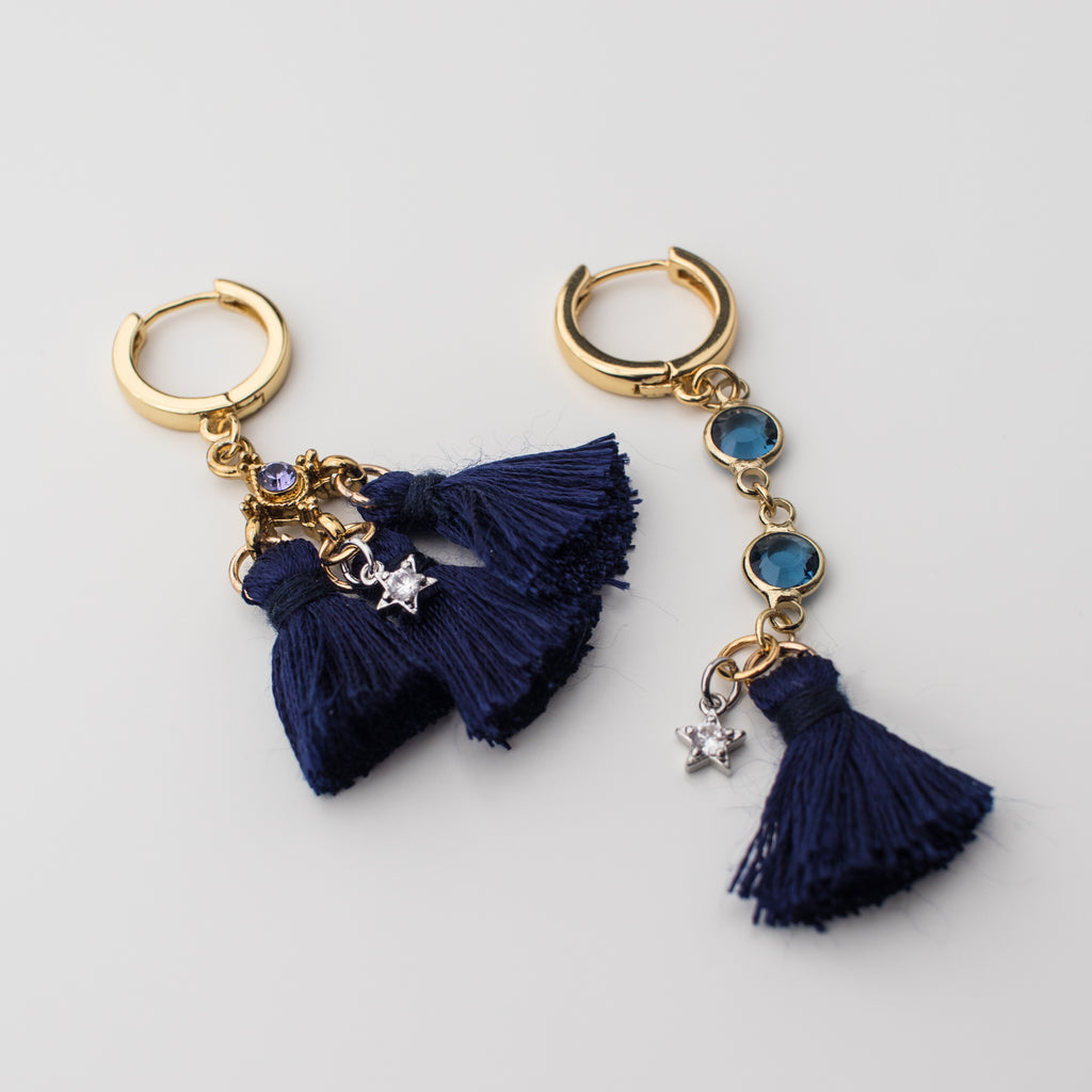 Gold hoop earrings with navy silk tassels and silver stars in a mismatched style.