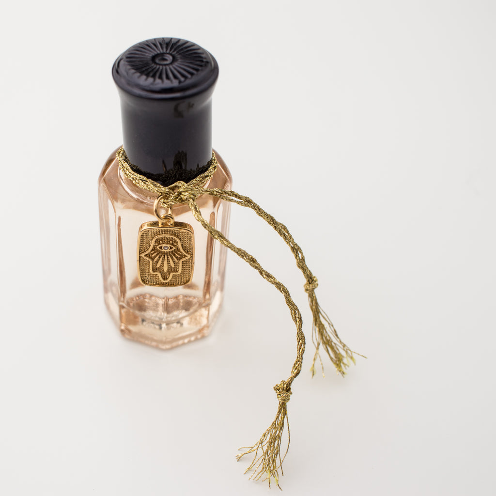 Amuletta's La Mûre fragrance. Blackberry, peach, jasmine, lavender & vanilla. In a blush bottle with a hamsa hand gold filled tag attached with gold braided embroidery thread.