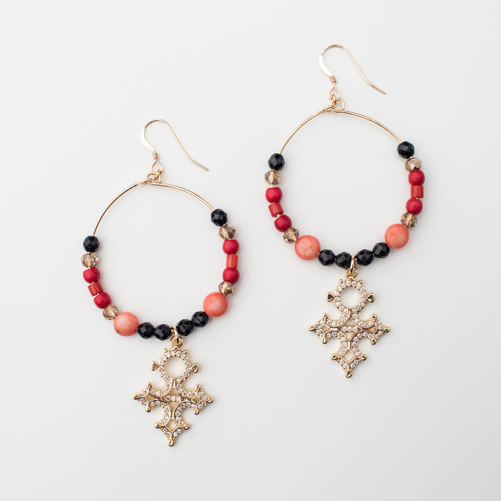 Large ornate gold cross hoops with red, apricot and black details in a matching style earring. 