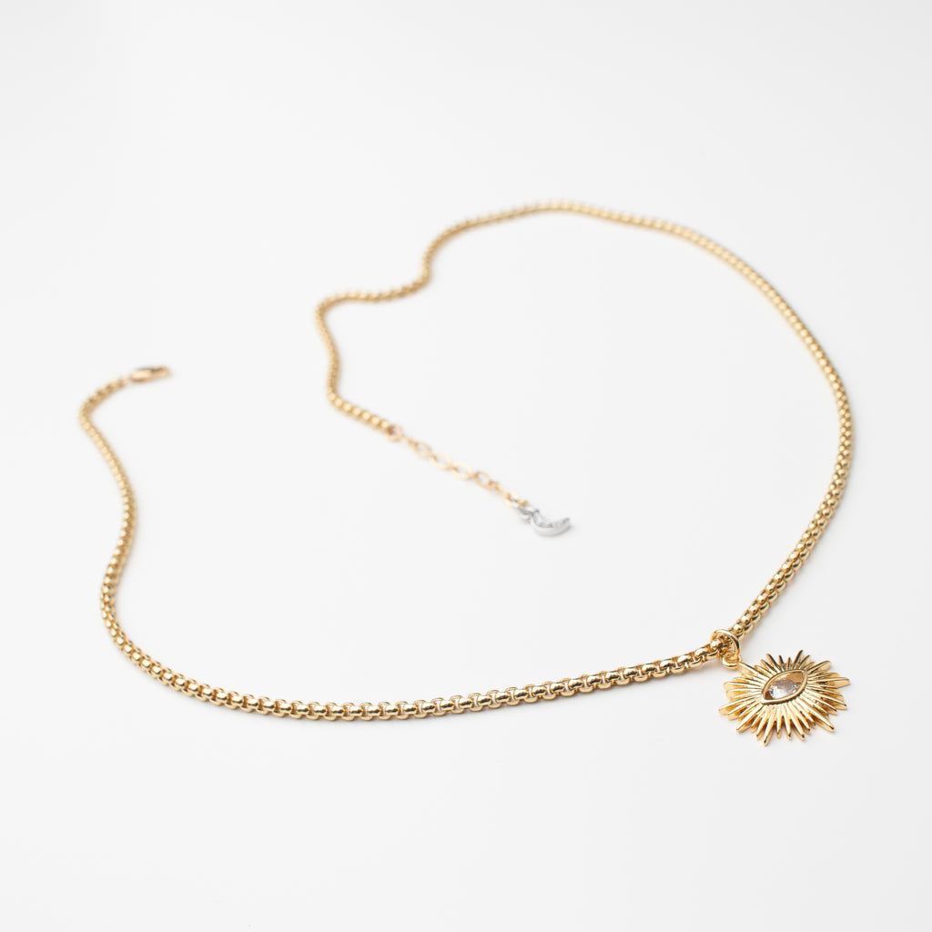 Gold sun pendant with a sparkly eye centre, on a gold chain with a silver zircon mini moon charm and a gold filled clasp. 