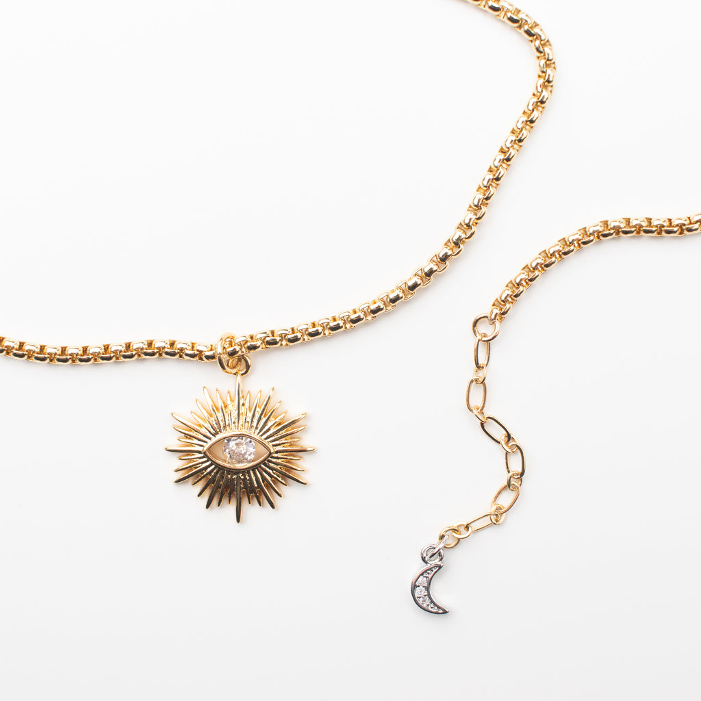 Gold sun pendant with a sparkly eye centre, on a gold chain with a silver zircon mini moon charm and a gold filled clasp. 