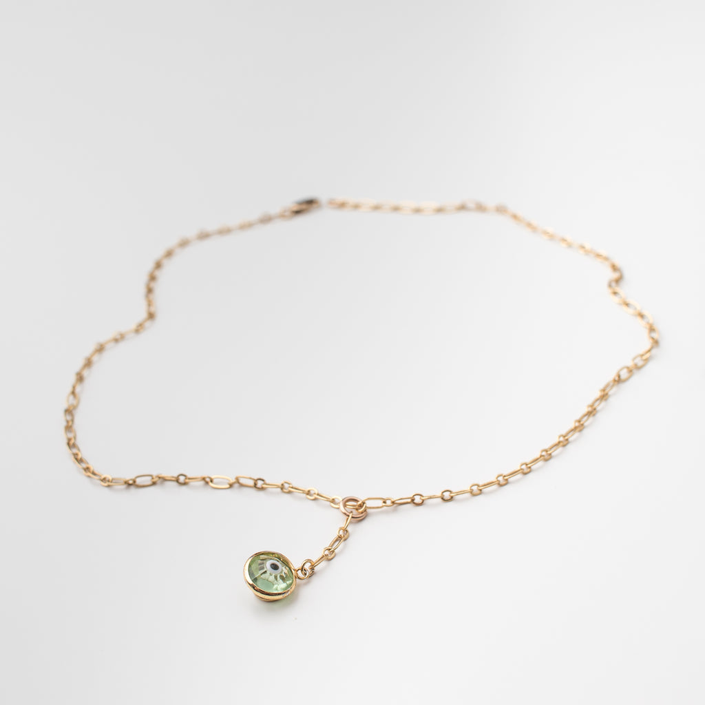Gold necklace with light green coloured crystal eye charm.