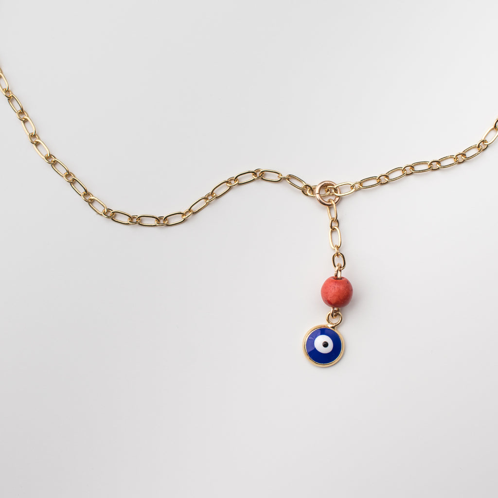 Gold necklace with an enamel cobalt blue eye charm and orange coral bead.